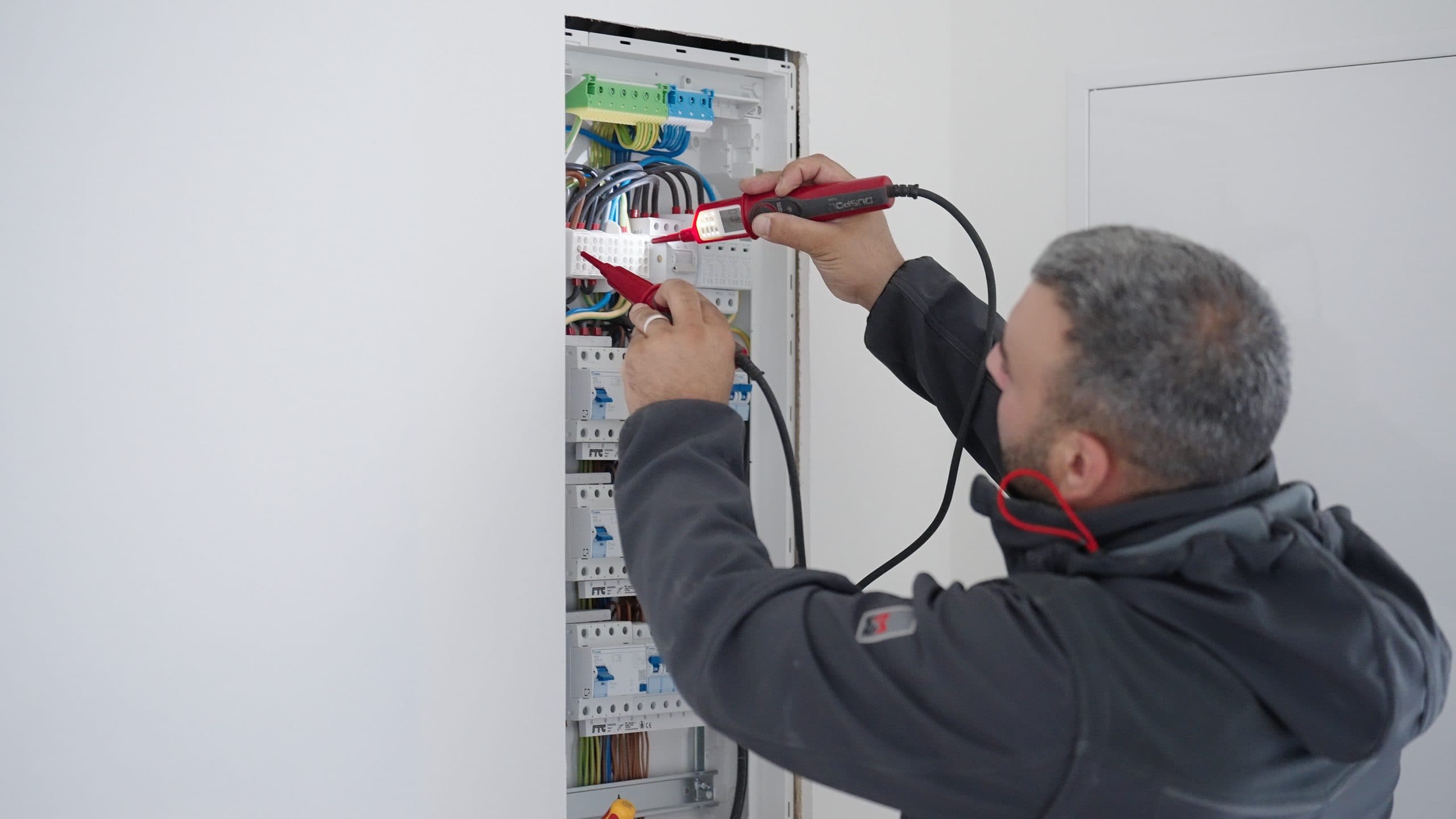 Elektriker prüft mit einem Spannungsprüfer die Verdrahtung in einem Verteilerschrank