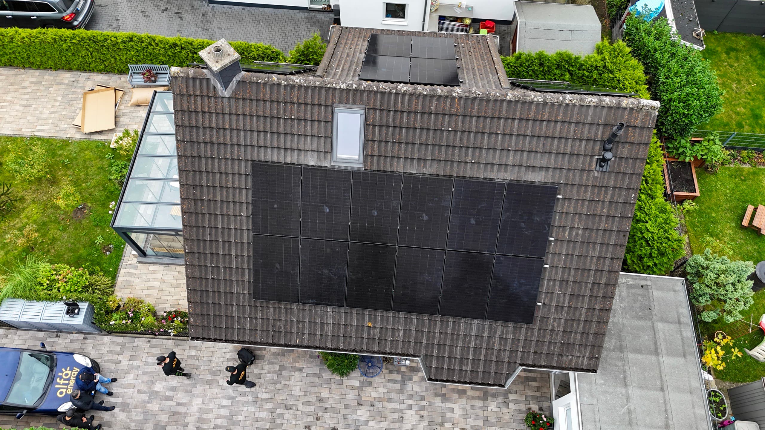 Drohnenaufnahme: Team von Alfa Energy und Firmenwagen im Hof vor einem Haus mit frisch installierter Photovoltaikanlage